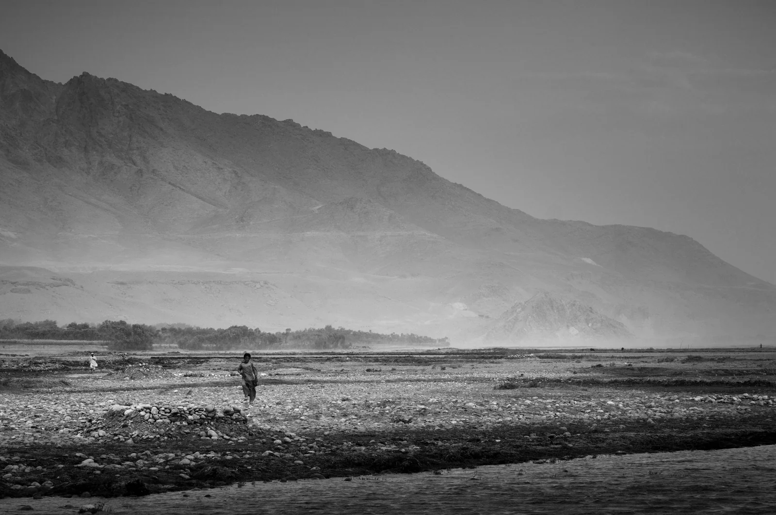 People crossing a broad river valley below mountains in Mahmood Raqi District, Kapisa.