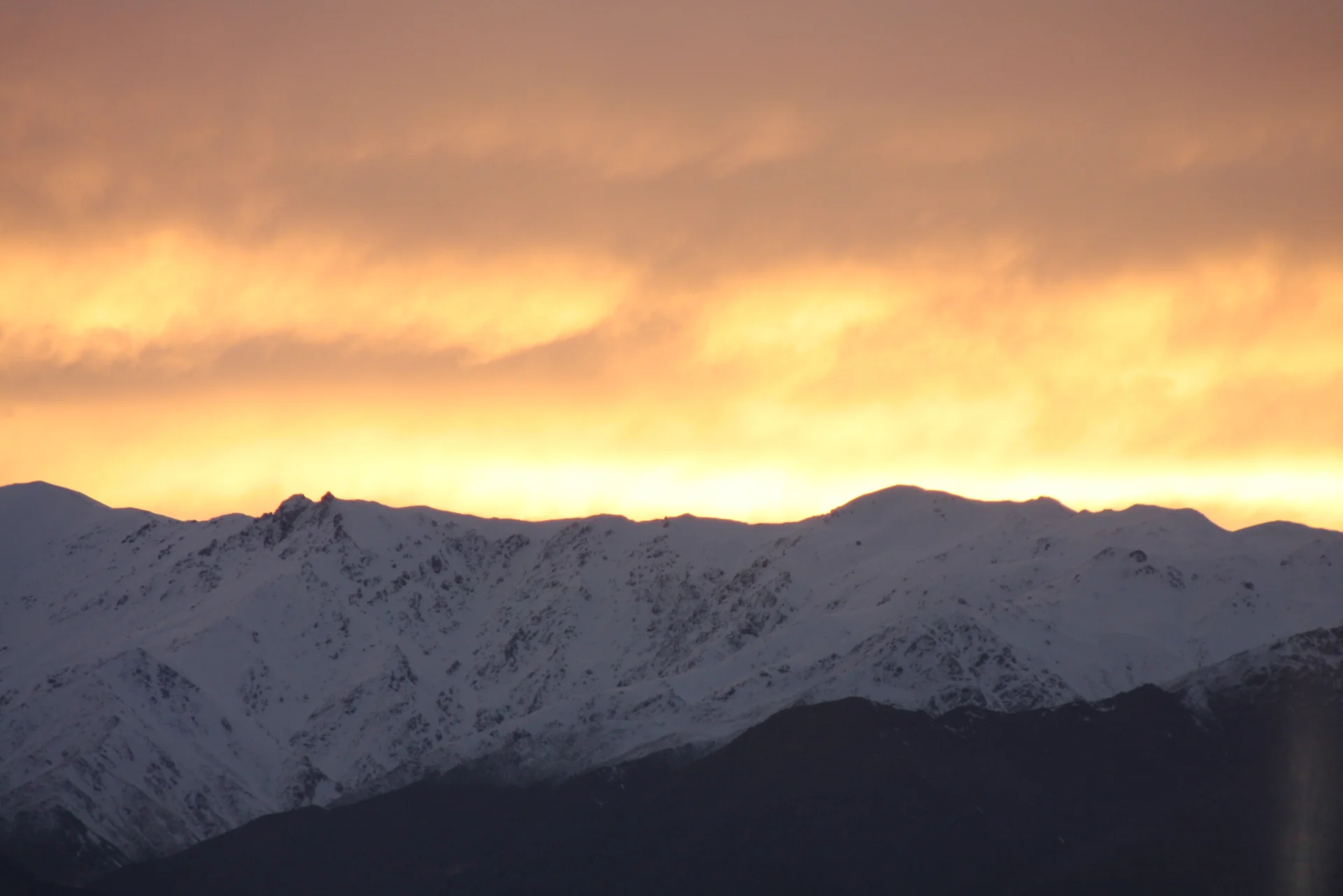 Snow-covered mountains in Parwan beneath a golden sunset sky.